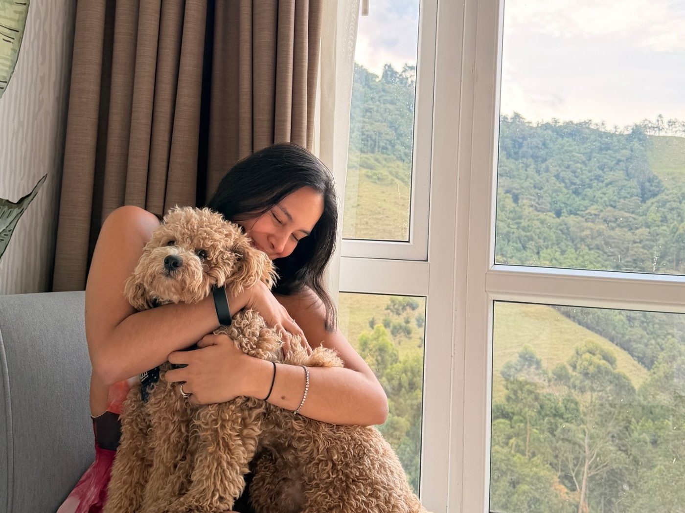 Cami abrazando a su perro junto a una ventana con vista a las montañas